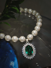 Luxury white pearl dog collar necklace with oval emerald green crystal pendant, pet jewelry for small dogs, dark background with green plant decor