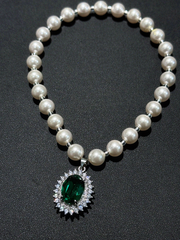 Full loop view of elegant pearl pet necklace, large emerald gem pendant surrounded by sparkling rhinestones, black background flat lay