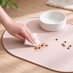 ands wiping spilled pet kibble off pastel pink silicone pet feeding mat, easy to clean for cat dog food bowl